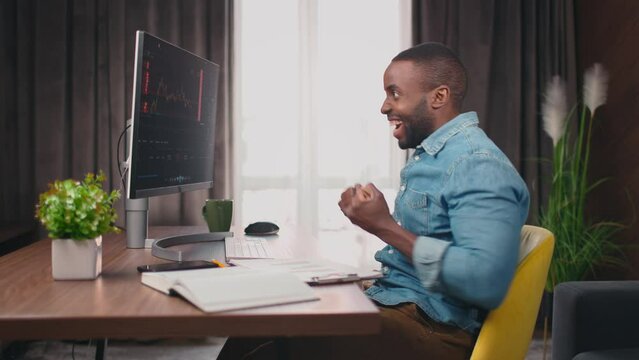 Side view shot of african american trader typing, checking diagrams on sceen and smiling celebrating victory. Happy people concept. Crypto currency trader. Graphs analysis, stock market. 4k. Office