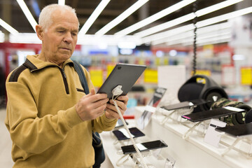 Naklejka na ściany i meble elderly man examines tablet computer in showroom of electronics store