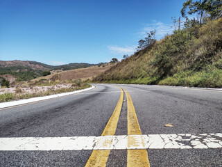 Close up road showing landscape background with mountains and hills and clear blue sky. Highway BR MG120 that connects the cities of Itabira and Nova Era Minas Gerais Brazil
