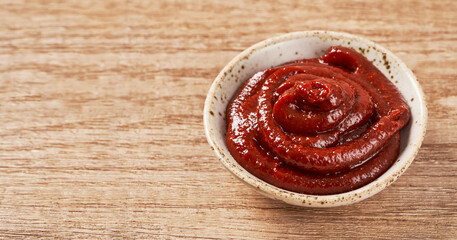 Gochujang or Korean red chili paste in a ceramic bowl on wood background. red chili sauce gochujang...