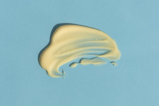 Yellow Cream Texture On A Blue Background. A Smear Of A Cosmetic Skin Care Product. Wellness And Beauty Concept. Top View