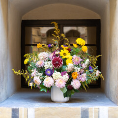 Bouquet of wild flowers and annuals in vase at window sill of historic building