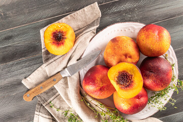 Ripe peaches with thyme leaves in a plate on a wooden board on a background