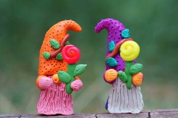 Two fabulous dwarfs are holding flowers. Toys made of plasticine.