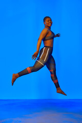 Happy african american woman wearing sportive clothes showing plus size hips. Body positive concept. Blue light on background
