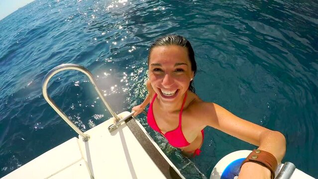 Excited woman emerging from the ocean onto a yacht and giving the peace sign