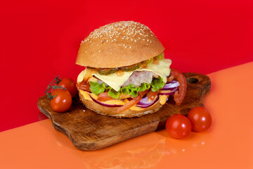 Delicious burger on the board with cutlet, tomatoes and cheese, cucumber and lettuce. On a red background. Fast food.