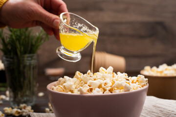 Melted butter being poured on popcorn in clay bowl on kitchen table