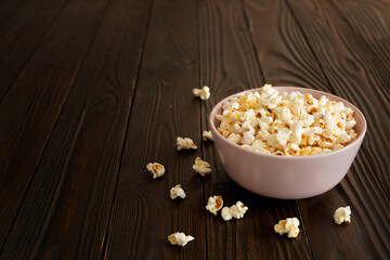 Bowl with popcorn on dark wooden table with copy-space