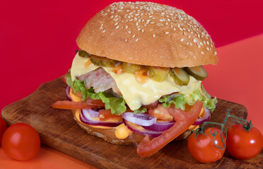 Delicious burger on the board with cutlet, tomatoes and cheese, cucumber and lettuce. On a red background. Fast food.