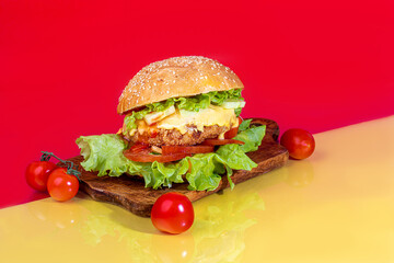 Delicious burger on the board with cutlet, tomatoes and cheese, cucumber and lettuce. On a red background. Fast food.