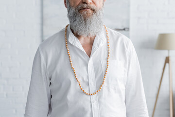 cropped view of bearded guru man in white shirt and beads at home. - obrazy, fototapety, plakaty