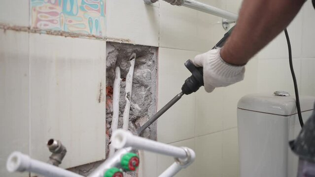 Construction worker breaks the concrete with a large hammer drill. A repairman breaks the old ceramic tile with a demolition hammer in bathroom. Home renovation and building new house concept