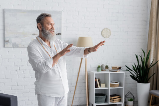 bearded guru man in white shirt meditating with outstretched hands at home.