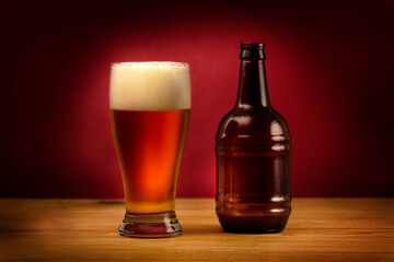 Glass of beer and a bottle on a wooden table and dark red background. Craft beer of local brewery. Focus is on the glass with beer.