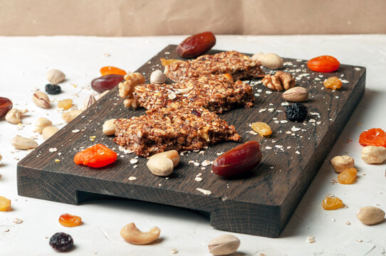 bar with flakes, nuts and dried fruits on a brown wooden board with ingredients scattered side by side on a gray background. the bars lie side by side with each other, side view.