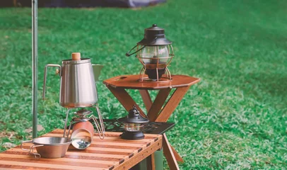  Selective focus at stainless steel kettle, portable gas stove, bowl and vintage lanterns on outdoor wooden table in camping area © Prapat