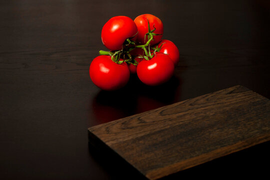 empty dark wooden cutting board, side view, copy space. in the background is a bunch of red tomatoes.