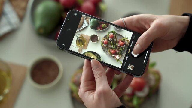 Closeup of female hands holding smartphone and taking pictures for social media in kitchen, cooking dietary meal from fresh vegetables and toasts. healthy eating concept. Vertical shoot. 4k footage