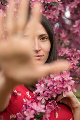 Portrait of a young woman with her hand outstretched in a blooming apple orchard.
