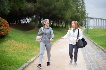 Fototapeta premium Content senior friends talking in park. Women in sportive clothes communicating on cloudy day. Sport, friendship concept