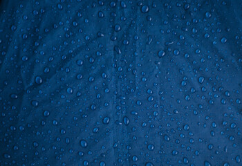 Rainwater drops on a blue background made of waterproof fabric. Texture and abstract background.