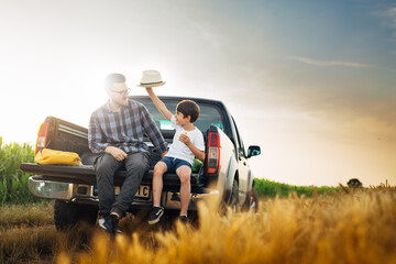 father and son checking wheat field outdoor. they are sits on truck of car - Powered by Adobe