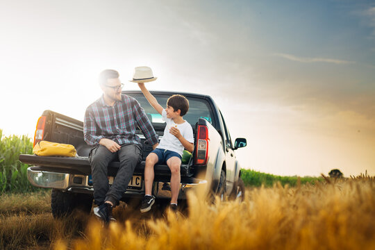 father and son checking wheat field outdoor. they are sits on truck of car
