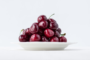 A mound of cherries on a white plate. Appetizing berries on a white background. Vitamins and a healthy lifestyle
