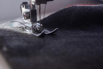 black fabric with a black thread on a sewing machine, the large foot of the machine lies on the fabric