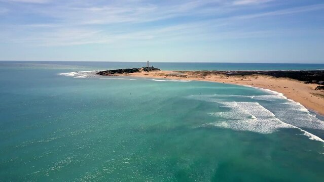 unique drone shoot over Ca&ntilde;os de Meca beach in Cadiz ,Spain where the drone glides to the beach and shows us the sea with some surfers, the waves and the lighthouse during a sunny summer day