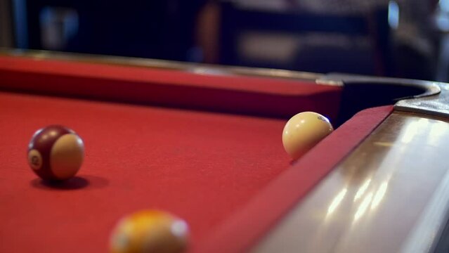 close up shot of a pool table where a player pushes the stick and hits the 8 ball into the hole in the red baize during an indoor day