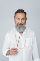 bearded healing guru holding aroma stick and looking at camera isolated on grey.