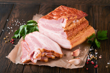 Whole Smoked Slab Bacon. Brisket. Sliced smoked gammon on a wooden table with rosemary, parsley, pepper, salt, and garlic on wooden stand and old table. Copy space.