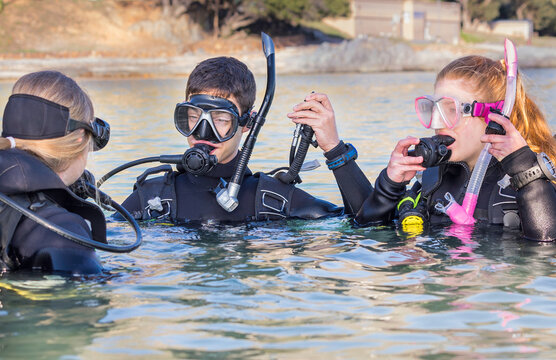 Scuba divers training in the sea looking at their instructor getting ready to submerge with their dive masks on and their deflator hoses lifted up