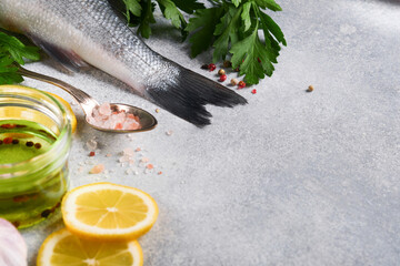 Fresh fish. Sea Bass raw with salt, pepper, parsley, olive oil and lemon on cutting board on light gray concrete rustic background. Food cooking background. Top view, copy space.