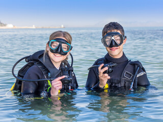 Smiling scuba divers in the sea, facing the camera with their dive masks on and their regulators in...