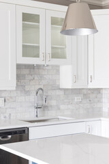 A kitchen sink detail shot with white cabinets and a marble subway tile backsplash.	