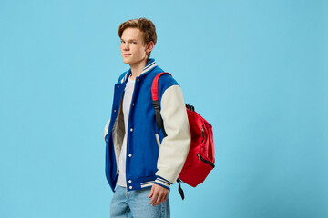 student with a backpack on his shoulder posing on a blue background