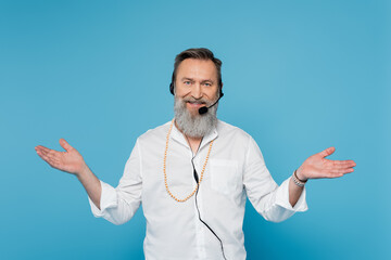 smiling motivational coach in headset standing with open arms isolated on blue.