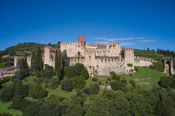 Fototapeta na wymiar Soave castle aerial view Verona province, Italy. Ancient castle on a hill in Italy. Italian flag on the main tower of Soave Castle. View of Soave castle surrounded by vineyard plantations.