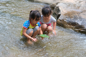 Happy cute little girl and her sister playing water in the stream. Little Asian sister enjoys swimming in the river. Healthy Summer Activities for Kids.