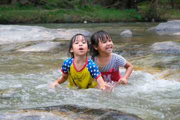 Happy cute little girl and her sister playing water in the stream. Little Asian sister enjoys...