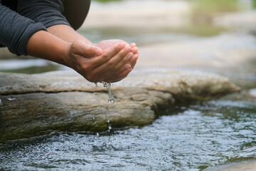Woman scooping clean water in the river by hands. Close-up of a woman holding hands in a clean...