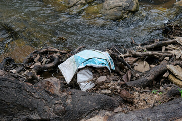 Many plastic waste between twigs and other organic materials are piled up along the riverbank. Pollution in the river