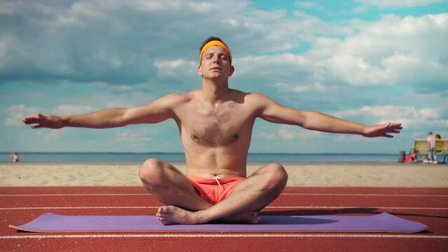 Funny fitness guy doing yoga in the background of the beach. Young guy doing fitness on a mat on the playground. Relax Lifestyle