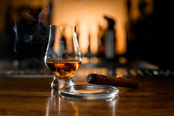 Selective focus on smoking cigar and glass with whiskey on blurred bar background