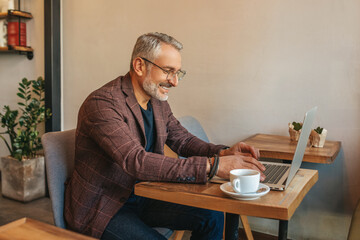 Man sitting sideways to camera working on laptop - obrazy, fototapety, plakaty