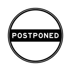 Black color round seal sticker in word postponed on white background