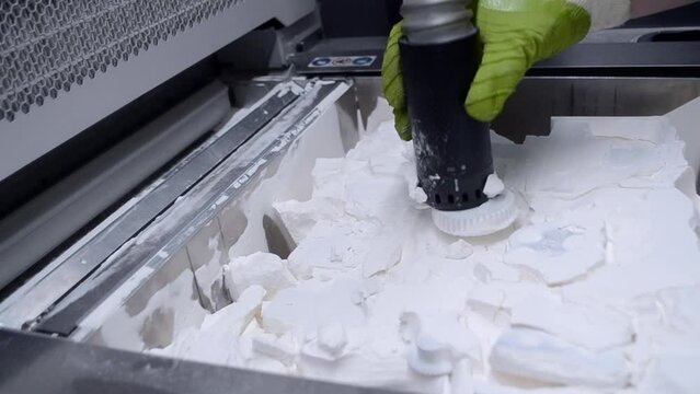 A man working with a working vacuum cleaner to clean the white powder of polyamide from a model printed on a 3D printer inside a 3D printer. Cleaning objects printed on an industrial powder 3D printer